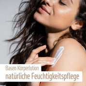 Eine Frau mit langen braunen Haaren trägt weiße Lotion auf ihre Schulter auf. Der Text auf dem Bild lautet: fitne Basische Körperlotion, mit Bio-Mandelöl für natürlich mit Feuchtigkeit versorgte Haut.
