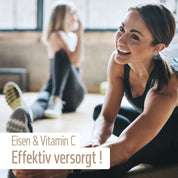 Zwei Frauen in Sportbekleidung dehnen sich in einem hellen Raum auf Yogamatten. Eine lächelt, während sie nach ihrem Fuß greift. Der Text auf Deutsch lautet: Eisen Komplex Kapseln von fitne – Organisch gebundenes Eisen & Vitamin C für effektive Versorgung!.