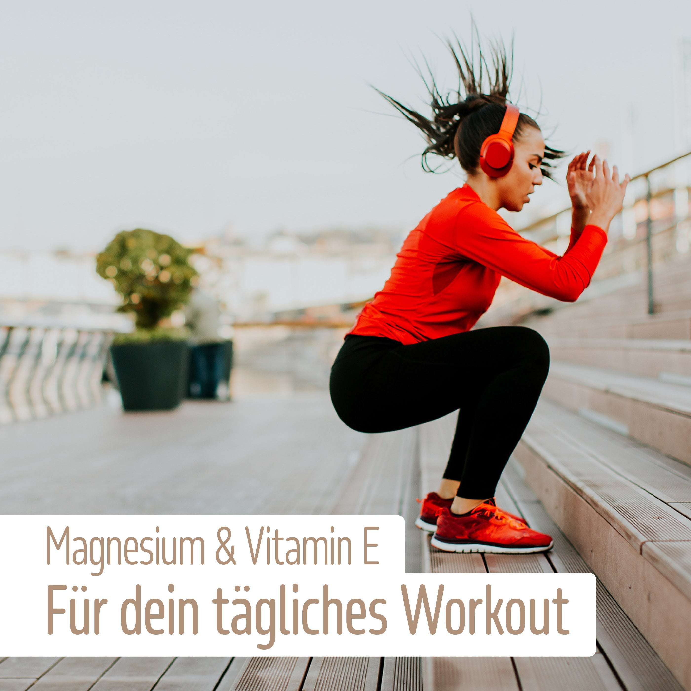 Eine Frau in Sportkleidung und roten Kopfhörern macht Squat-Sprünge auf Außentreppen. Deutscher Text: „Magnesium + Vitamin E Kapseln von fitne – für deinen Energiefluss beim täglichen Workout.“.