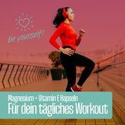 Eine Frau in roter Sportkleidung mit Kopfhörern trainiert an einer Strandpromenade. Der deutsche Text hebt FITNE Health Care Magnesium + Vitamin E Kapseln für den Energiestoffwechsel beim täglichen Training hervor. Ein Herzsymbol und "Sei du selbst!" sind abgebildet.