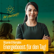Eine selbstbewusste Frau steht mit verschränkten Armen und lächelt. Der Text lautet "Sei du selbst!" mit einem Herz, und darunter FITNE Health Care Vitamin B Komplex Kapseln mit natürlichen B-Vitaminen für deinen Energiestoffwechsel auf orangem Banner. Unscharfe Menschen im Hintergrund.